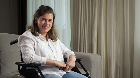 Disabled Woman Smiles Sitting in Wheelchair By Sofa at Home