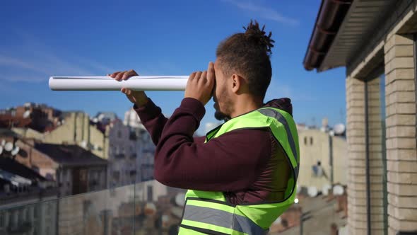 Side View Young African American Man in Vest Using Rolled Blueprint As Spyglass Outdoors