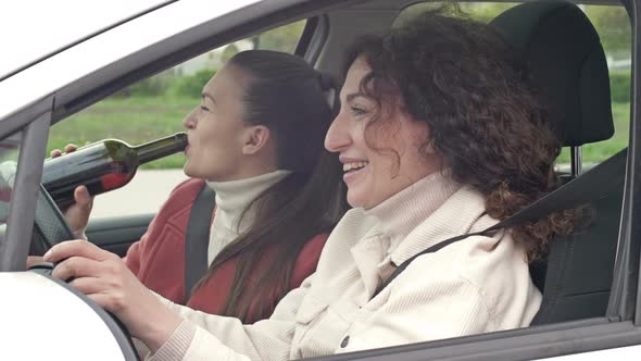 Two Girlfriends Drink Wine From a Bottle While Sitting in the Car