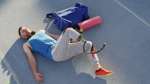 Caucasian disabled male athlete with running blade wearing headphones and stretching