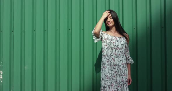 Pretty Brunette in Light Dress Poses with Hair on Background During Wind