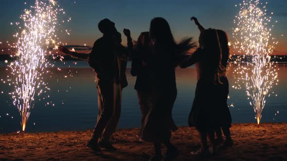 Happy Youth Girls and Guys Having Fun on Beach at Night Dancing and Enjoying Fireworks