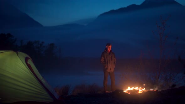 Alone Tourist Standing Near Tent and Looking at the Campfire