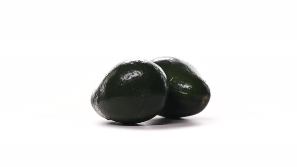 Two Dark Green Avocados Spinning on White Background