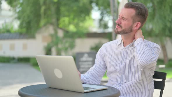 Middle Aged Man with Laptop Having Neck Pain in Outdoor Cafe