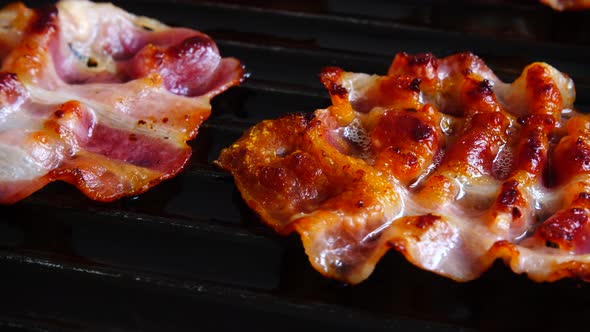 Fried bacon slices rotate in a grill pan.