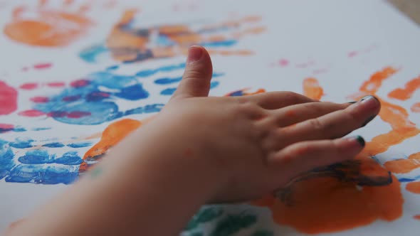 Little Girl with Paints on Her Hands Draws on White Paper
