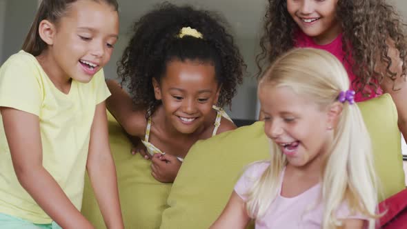 Video of diverse girls sitting at school common room with tablet, talking and laughing