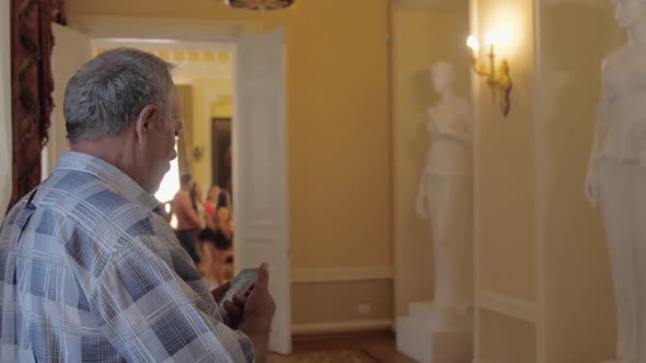 Pensioner Holds Smartphone and Takes Photo in Museum Castle