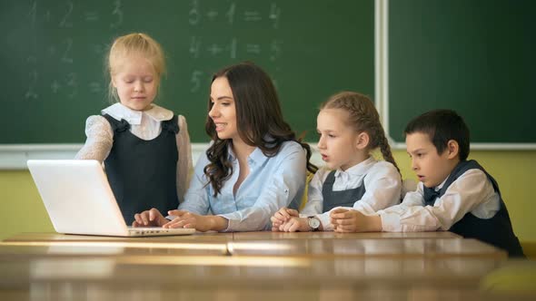 Happy Teacher Using Laptop with Pupils in the Classroom