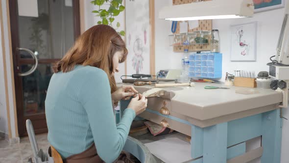 Back View Of A Female Jewelry Maker Filing A Piece Of Jewellery In A Workshop