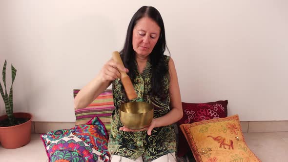 Middle age woman using bronze Tibetan singing bowl. Concept of relax and zen aura.