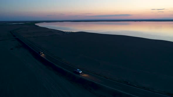 Aerial View of Car Driving on an Empty Road in the Desert Next To the Lake During Sunset