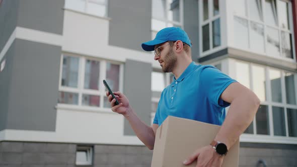 A Male Mail Carrier with Round Glasses Carries Boxes for Delivery to Customers and Looks at His