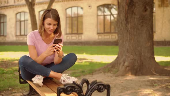 Young Woman Messaging on Mobile Near College