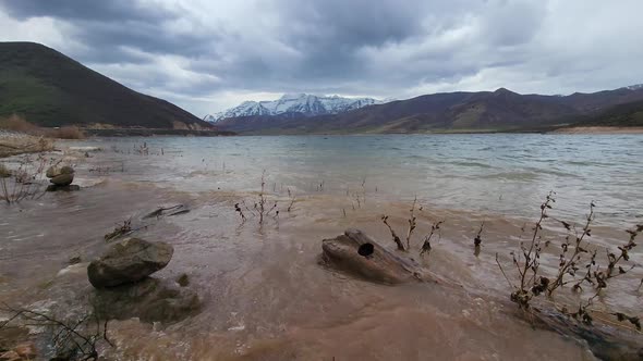 Panning view of muddy water waves lapping on shore of Deer Creek Reservoir