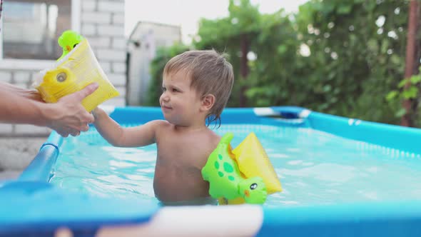 Mom Puts a Sleeve on the Arm of a Naked Baby Who Plays in the Pool in the Yard
