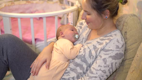 Young Mother Puts Her Baby To Sleep in Her Arms. Breastfeeding Baby Lies with Mom in Her Arms