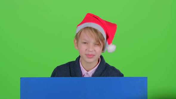 Youngster Boy Appeared From Behind a Blue Poster Points To His Index Fingers. Green Screen