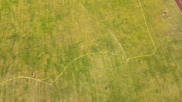 Top down aerial view of football field surface covered with green grass and sprinklers spraying