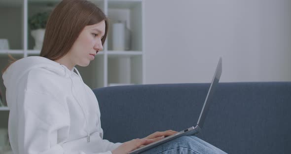 Woman Using Laptop on Couch at Home. Thoughtful Young Woman Sitting with Computer on Couch, Looking