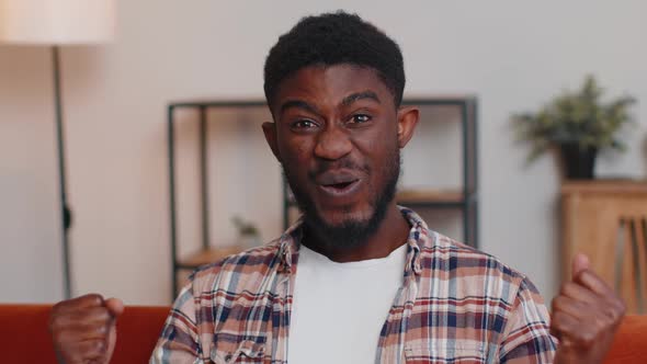 Excited Amazed African American Man Raising Hands in Surprise Shocked By Sudden Victory at Home Sofa