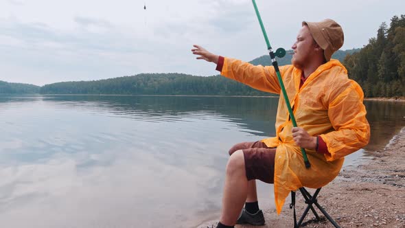 Lonely Man in Orange Raincoat Sitting on a Shore and Smoking a Cigarette on Fishing