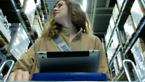 Beautiful Woman Is Looking in the Storehouse for Her Goods Using a Tablet Computer Pc