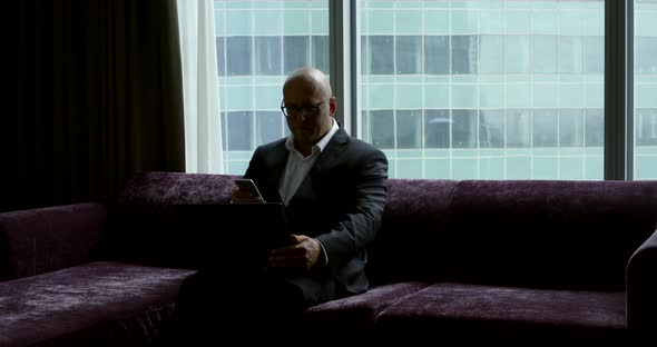 Silhouette of a Businessman in Front of the Window Sitting on the Couch in a Suit and Work for the