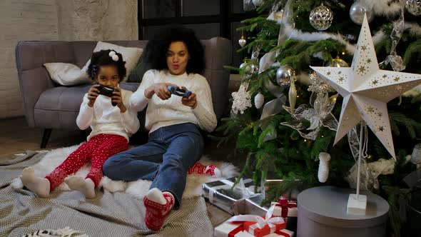 Portrait of African American Mom and Her Little Daughter Playing the Game with Joysticks and
