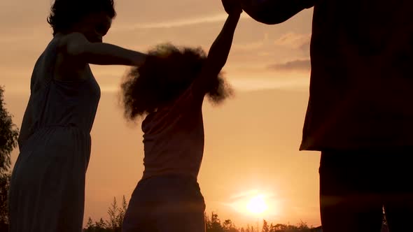 Silhouettes of Parents Having Fun with Their Little Daughter Against Sunset