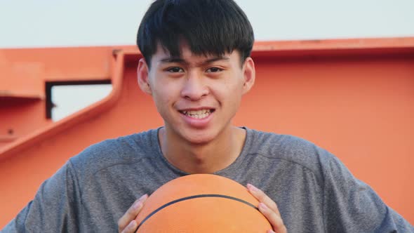 Young basketball player sitting on the edge of the court holding a ball smiles at the camera while