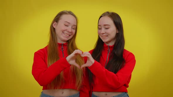 Female Caucasian Twins Making Heart Shape with Hands Looking at Camera Smiling