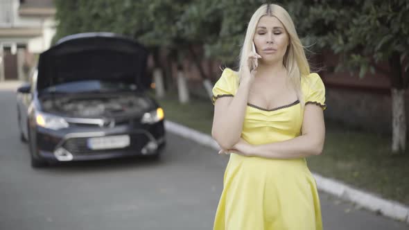 Portrait of Beautiful Slim Blond Caucasian Woman in Yellow Dress Complaining Car Breakage on the