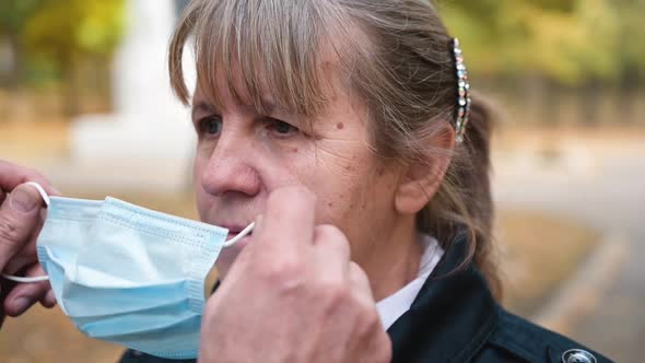 Senior Caucasian Man Helps Puts a Medical Mask on the Face of an Senior Woman