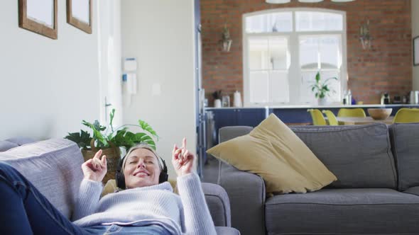 Relaxed senior caucasian woman in living room lying on sofa, wearing headphones