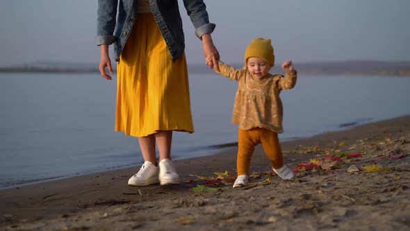 Mom Holds Her Daughter By the Hand and Teaches Her To Walk on Beach