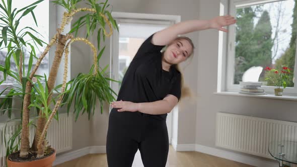 Positive Beautiful Plump Woman Bending Exercising at Home and Smiling Looking at Camera