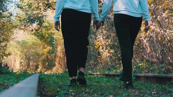 Twins Girls Holding Hands Walking Along Railroad Tracks