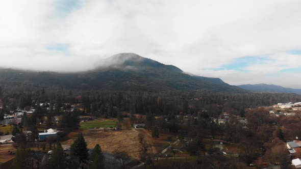 Aerial descending over small mountain town, cloud-covered mountain looming in background