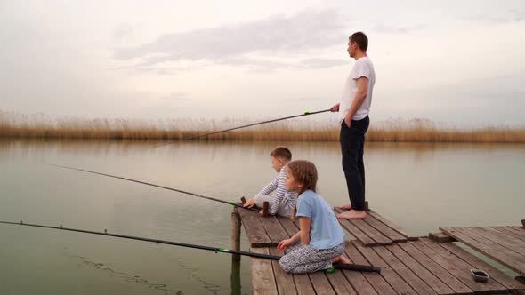 Dad and Son and Daughter on a Wooden Bridge Catch Fish From the River