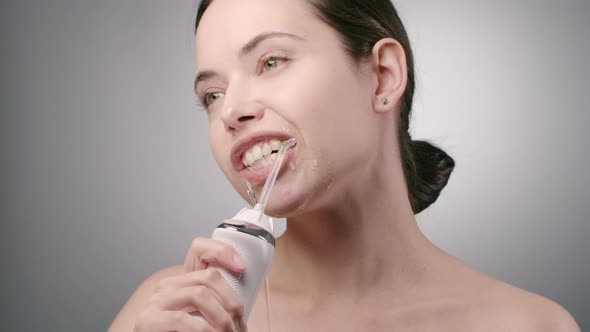 Young Woman with Dark Brown Hair Cleaning Teeth with Water Flosser and Smiling