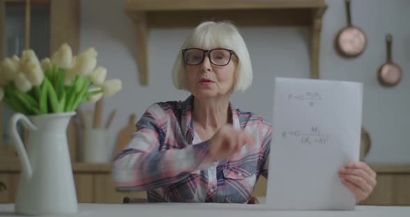 Senior Teacher in Glasses Showing Sheet of Paper with Physics Equations Looking at Camera