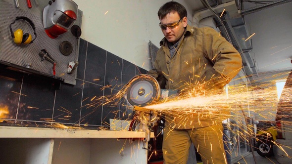 Worker using a grinder cuts metal in a workshop