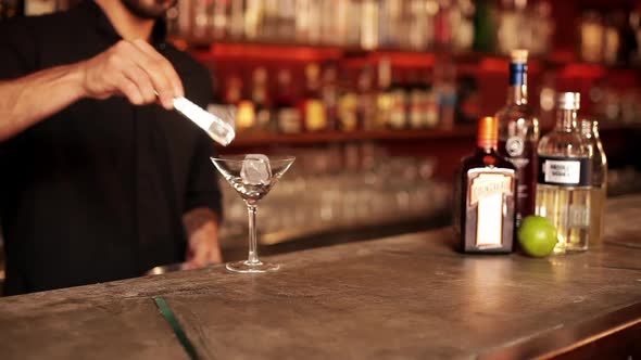 Bartender placing ice cubes in martini glass