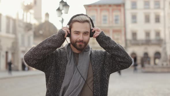 A Happy Bearded Man is Putting on Headphones and Looking at the Camera