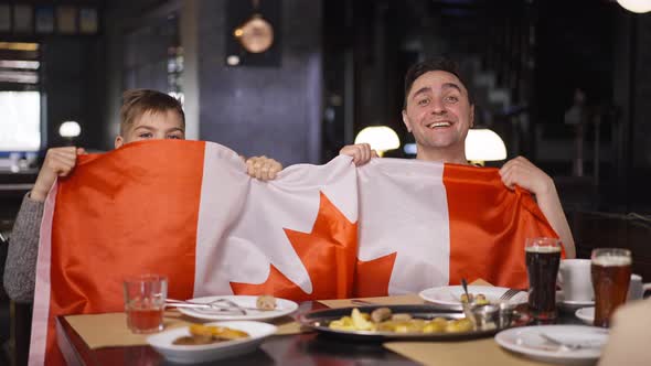 Front View Man and Boy with Canadian Flag Rejoicing Success Watching Hockey Match in Restaurant