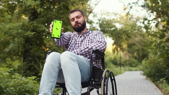 Caucasian Disabled Person Young Man is Sitting Wheelchair in Park Holding Phone with Chromakey on