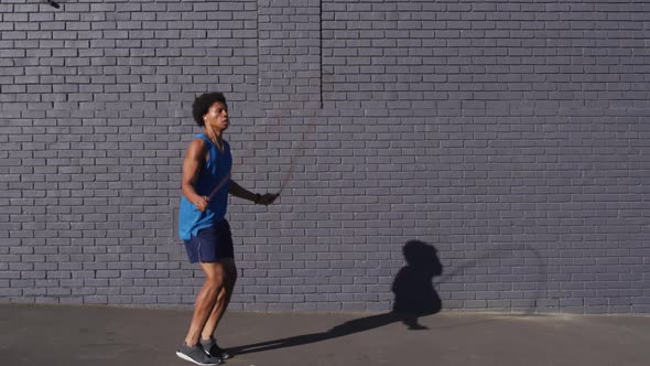 Fit african american man exercising in city, using earphones, skipping with skipping rope in street