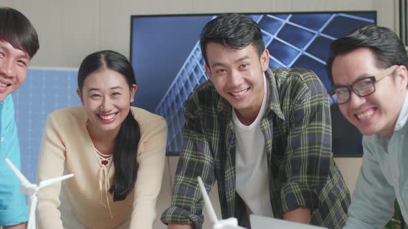 Asian Engineers Group Smiling To Camera While Working About Small House Model With Solar Panel